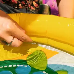 Ręka sprawdza szczelność dmuchanego basenu, szukając sposobu, czym skleić basen, by znów cieszyć się zabawą.