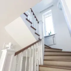 Jasne schody z drewnianymi elementami i białymi balustradami. Pomysł, jak tanio wykończyć schody betonowe, by wyglądały elegancko.