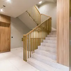 Nowoczesna zabudowa klatki schodowej w domu jednorodzinnym z drewnianymi elementami i złotymi balustradami. Obok winda.