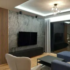 Nowoczesny salon z betonem architektonicznym, który świetnie komponuje się z drewnianymi lamelami i granatową sofą.