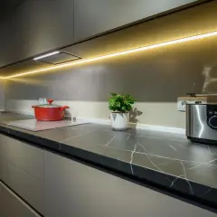 Nowoczesna kuchnia z eleganckim oświetleniem LED nad blatem. Czerwony garnek i toster dodają koloru. Idealne rozwiązanie, jak oświetlić kuchnię.