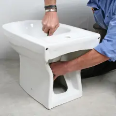 Instalator montuje białą ceramikę, pokazując, jak podłączyć bidetta.