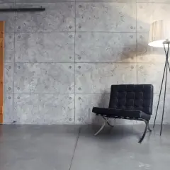 Drewniane drzwi przesuwne, czarny fotel i lampa stojąca na tle ściany z betonu dekoracyjnego.