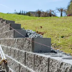 Budowa murek oporowy w ogrodzie. Betonowe bloki układane są warstwami, tworząc solidną konstrukcję.