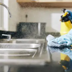 Rękawiczki i ściereczka pomagają w tym, jak wyczyścić zlew. Rozpylony płyn czyści blat kuchenny.