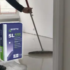 Pracownik rozlewa masę samopoziomującą Bostik SL G320, by wyrównać posadzkę.