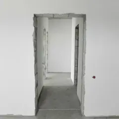 Niedokończony otwór drzwiowy, idealny do rozważań, jak zmniejszyć otwór drzwiowy o 10 cm. Betonowe ściany i surowe wykończenie.