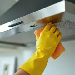 Ręka w żółtej rękawiczce czyści okap ze stali nierdzewnej pomarańczową ściereczką. Dowiedz się, czym wyczyścić okap ze stali nierdzewnej, by lśnił jak nowy.