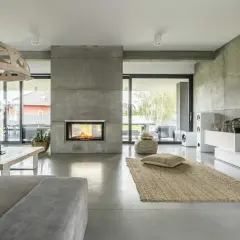 Nowoczesny salon z kominkiem i podłogą z betonu architektonicznego. To właśnie **co to jest mikrocement** – materiał imitujący beton, nadający wnętrzu surowy, ale elegancki charakter.