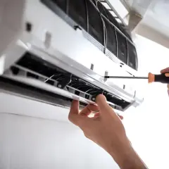 Serwis klimatyzacji w bloku. Ręce majsterkowicza przykręcają śrubkę w jednostce wewnętrznej klimatyzatora.