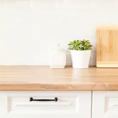 Drewniany blat kuchenny, białe płytki, ozdobny słoik, roślina w doniczce i deski do krojenia. Jak odnowić blat kuchenny z mdf?