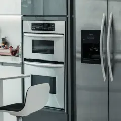 Nowoczesna kuchnia z lodówką obok piekarnika w zabudowie. Dwa stylowe krzesła barowe stoją przy blacie.