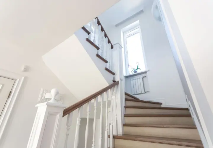Jasne schody z drewnianymi elementami i białymi balustradami. Pomysł, jak tanio wykończyć schody betonowe, by wyglądały elegancko.