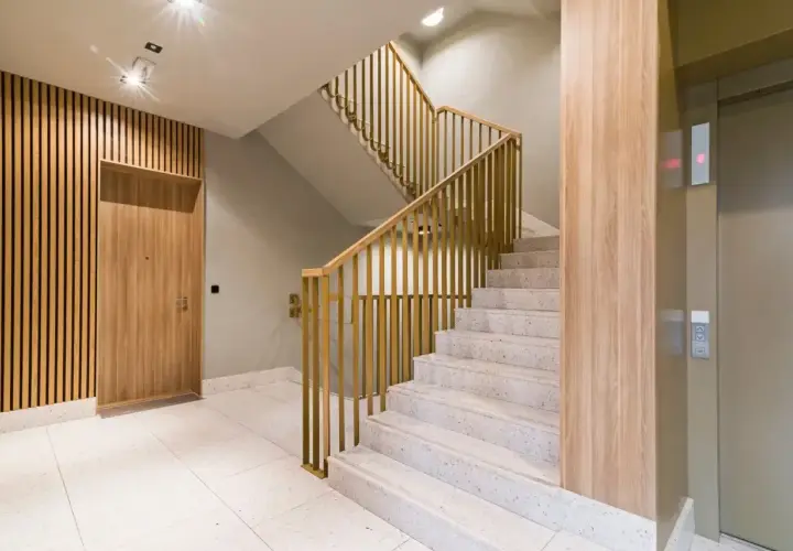 Nowoczesna zabudowa klatki schodowej w domu jednorodzinnym z drewnianymi elementami i złotymi balustradami. Obok winda.