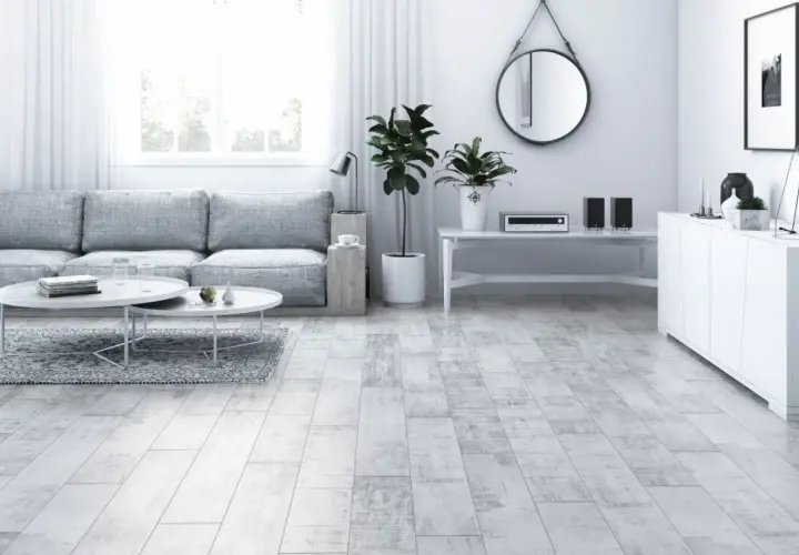 Jasny salon z szarą kanapą, białymi stolikami i podłogą imitującą drewno hikora.