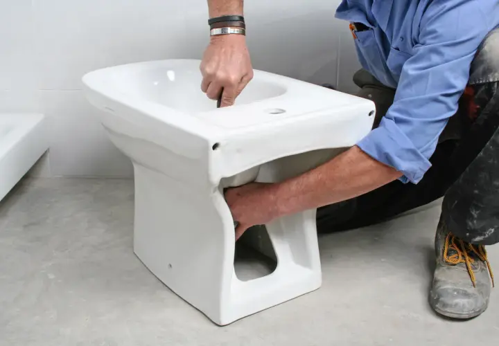 Instalator montuje białą ceramikę, pokazując, jak podłączyć bidetta.