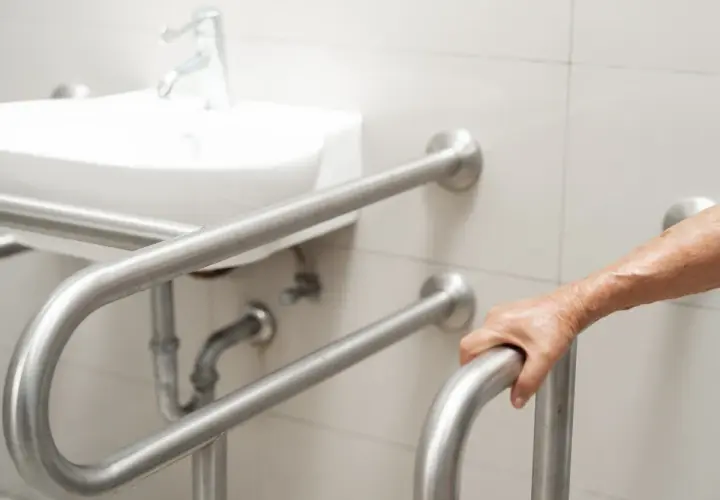 Dłoń osoby starszej chwyta uchwyt dla niepełnosprawnych. Łazienka przystosowana zgodnie z przepisami.