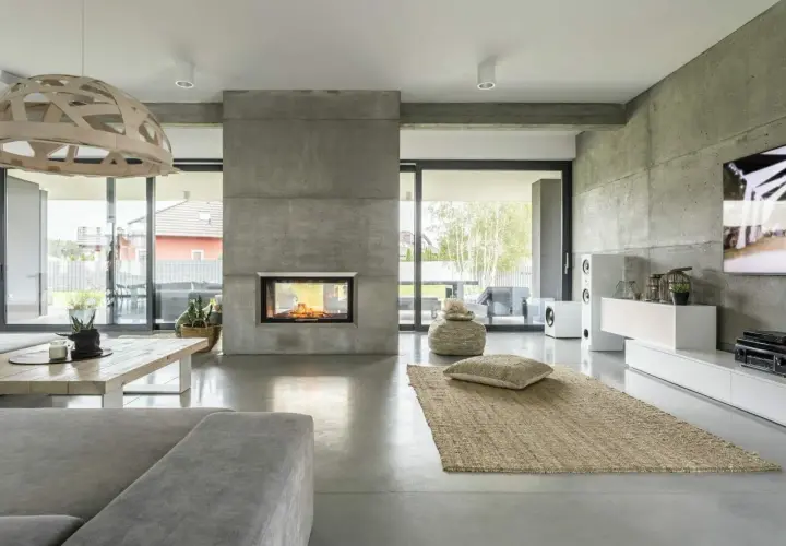 Nowoczesny salon z kominkiem i podłogą z betonu architektonicznego. To właśnie **co to jest mikrocement** – materiał imitujący beton, nadający wnętrzu surowy, ale elegancki charakter.