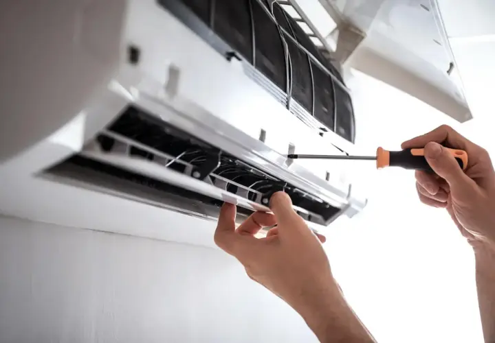 Serwis klimatyzacji w bloku. Ręce majsterkowicza przykręcają śrubkę w jednostce wewnętrznej klimatyzatora.
