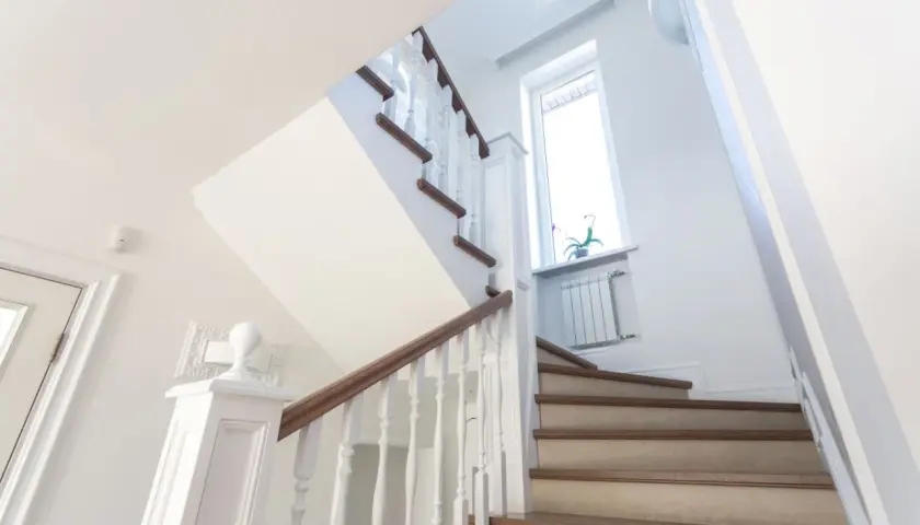 Jasne schody z drewnianymi elementami i białymi balustradami. Pomysł, jak tanio wykończyć schody betonowe, by wyglądały elegancko.