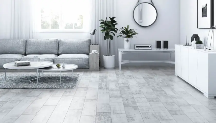 Jasny salon z szarą kanapą, białymi stolikami i podłogą imitującą drewno hikora.