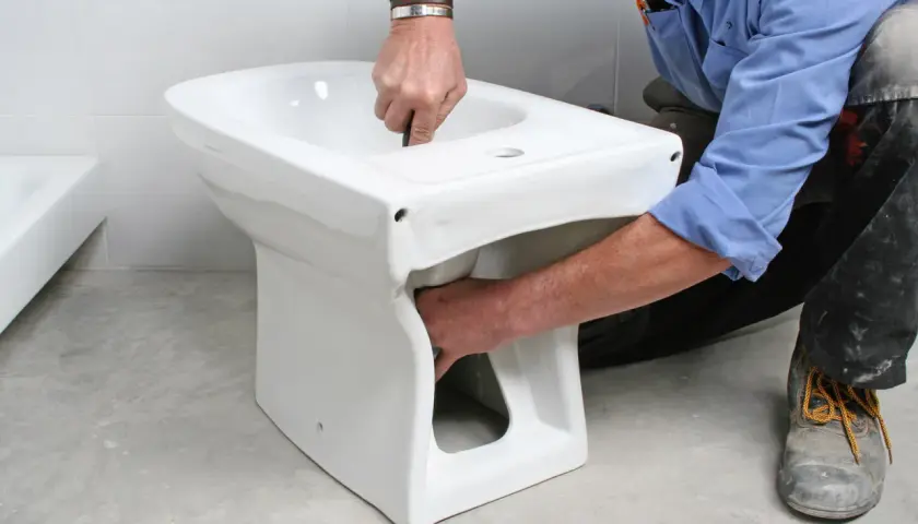 Instalator montuje białą ceramikę, pokazując, jak podłączyć bidetta.