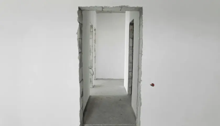 Niedokończony otwór drzwiowy, idealny do rozważań, jak zmniejszyć otwór drzwiowy o 10 cm. Betonowe ściany i surowe wykończenie.