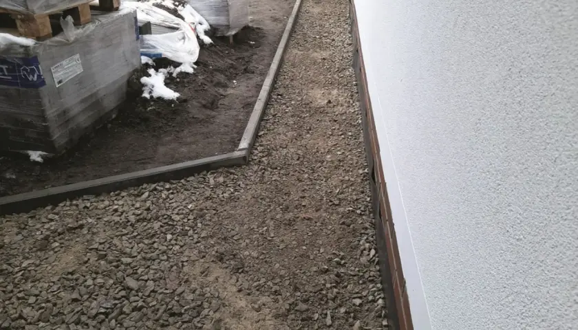 Niedokończony podjazd do domu, z paletami kostki brukowej i żwirem.