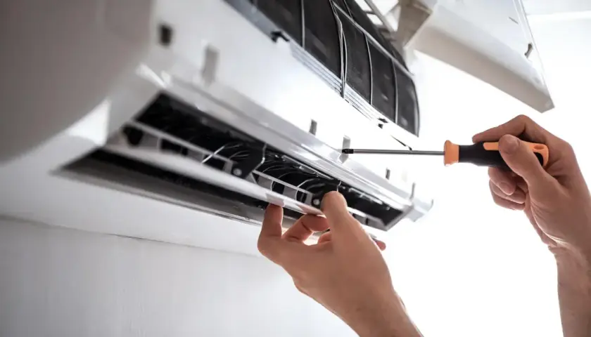 Serwis klimatyzacji w bloku. Ręce majsterkowicza przykręcają śrubkę w jednostce wewnętrznej klimatyzatora.