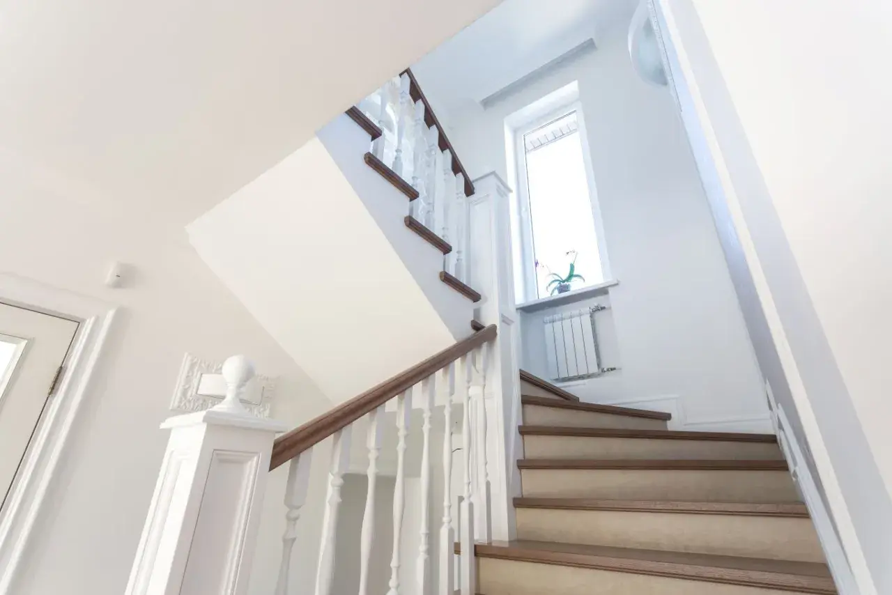 Jasne schody z drewnianymi elementami i białymi balustradami. Pomysł, jak tanio wykończyć schody betonowe, by wyglądały elegancko.