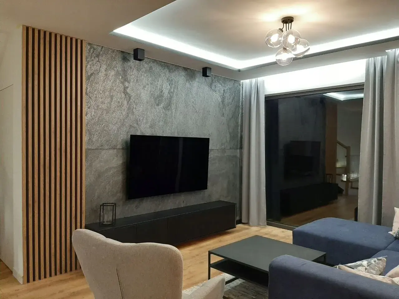 Nowoczesny salon z betonem architektonicznym, który świetnie komponuje się z drewnianymi lamelami i granatową sofą.