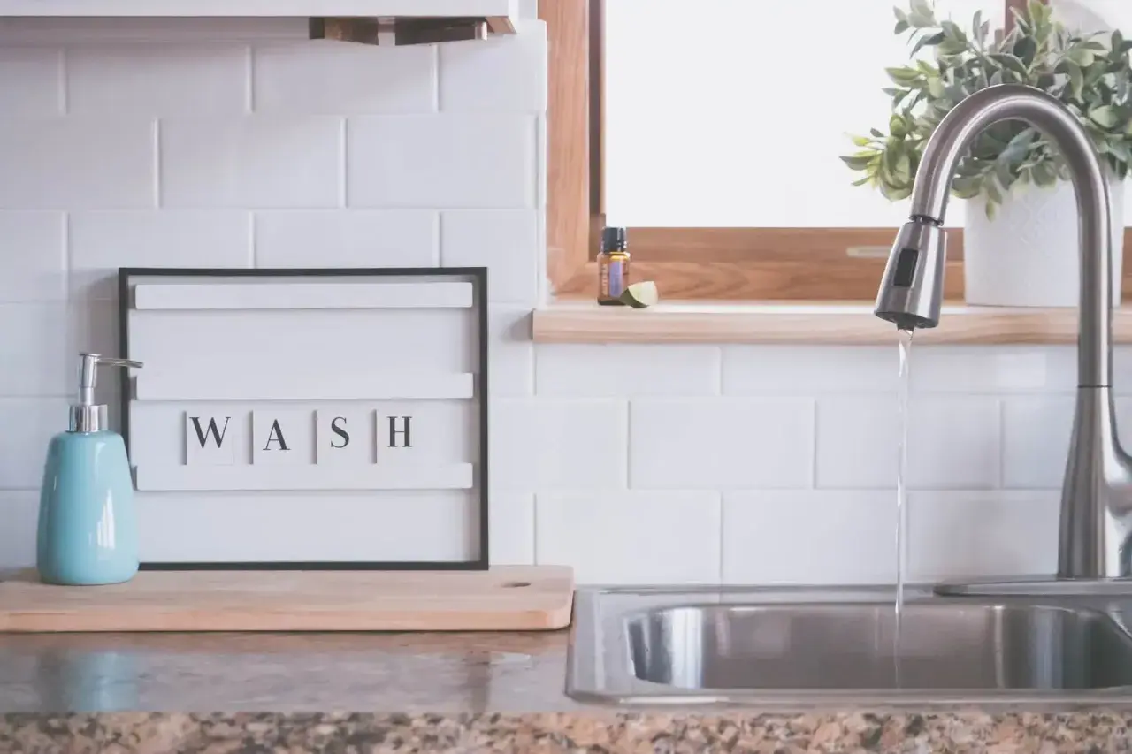 Napis "WASH" na tablicy między szafkami w kuchni, obok dozownika mydła i zlewu. Idealna inspiracja, co na ścianę w kuchni między szafkami.
