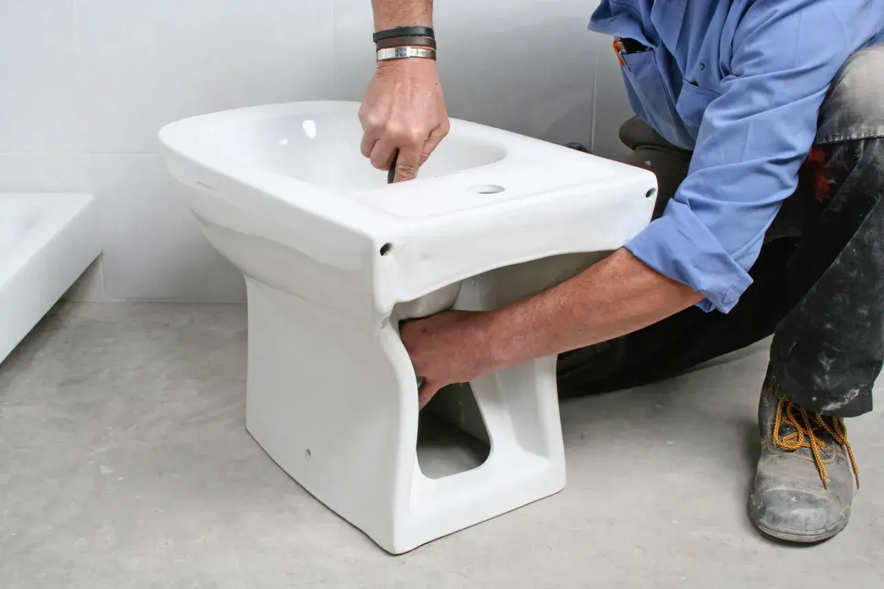 Instalator montuje białą ceramikę, pokazując, jak podłączyć bidetta.