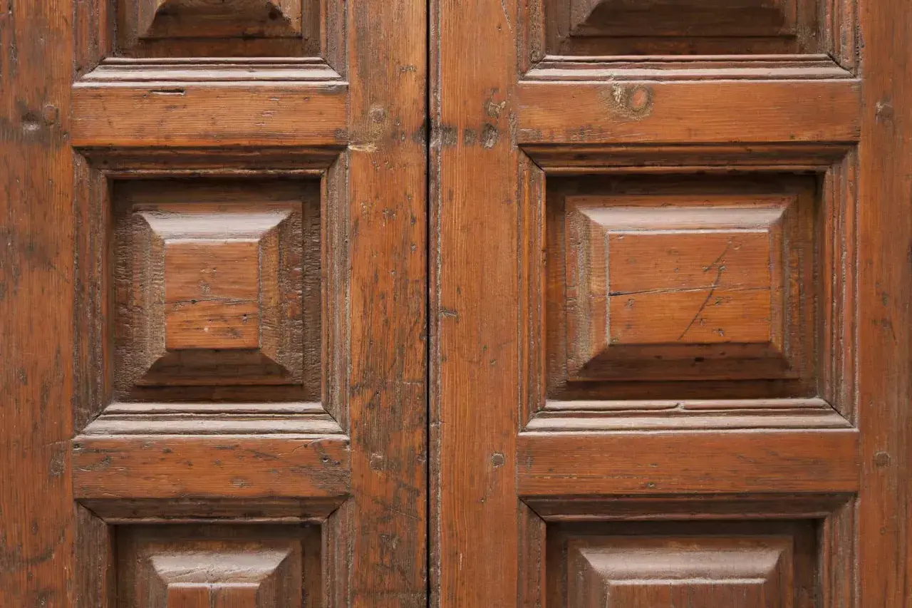 Renowacja drzwi drewnianych cennik: zbliżenie na zabytkowe, dwuskrzydłowe drzwi z widocznymi panelami i naturalnym usłojeniem drewna.