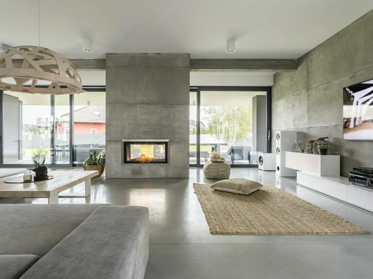 Nowoczesny salon z kominkiem i podłogą z betonu architektonicznego. To właśnie **co to jest mikrocement** – materiał imitujący beton, nadający wnętrzu surowy, ale elegancki charakter.
