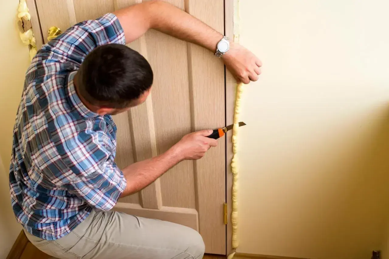 Mężczyzna przycina piankę montażową podczas wymiany ościeżnicy.