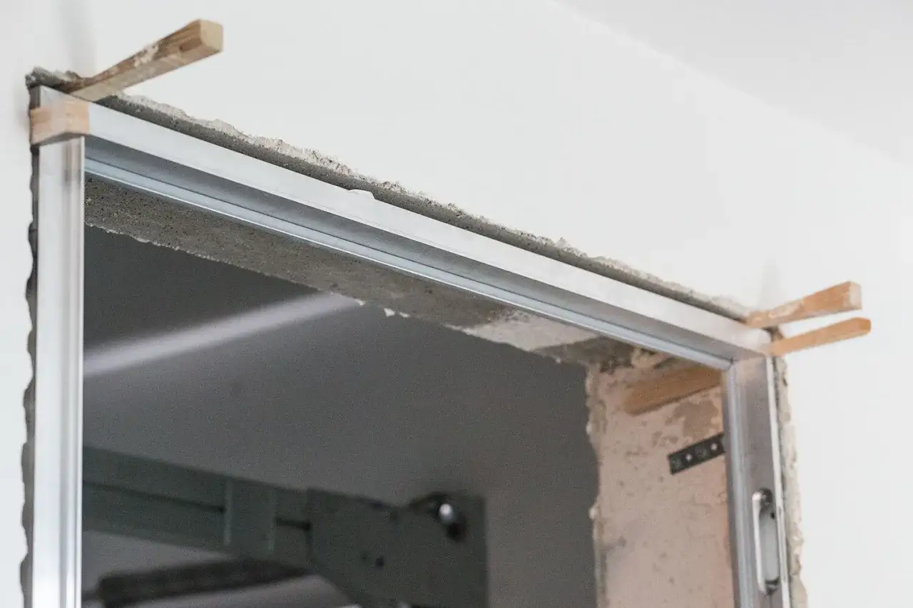 Montaż drzwi ukrytych cena: widok na otwór drzwiowy z profilem aluminiowym i drewnianymi klinami, przygotowanie do instalacji.