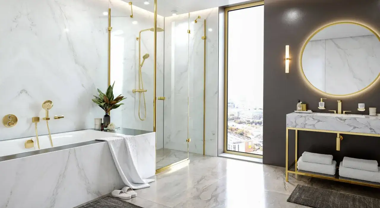 Luksusowa łazienka z armaturą Grohe i Hansgrohe w złotym wykończeniu. Marmurowe ściany i blat, wanna, prysznic i lustro z podświetleniem.