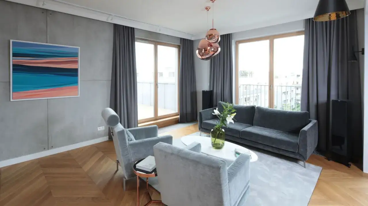 Nowoczesny salon z betonem architektonicznym na ścianie, szarymi meblami i drewnianą podłogą. Idealne połączenie z czym łączyć beton architektoniczny.